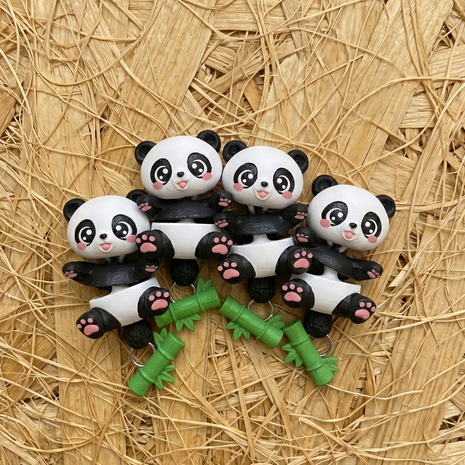 Four Flexi Baby Panda keychains on a straw background