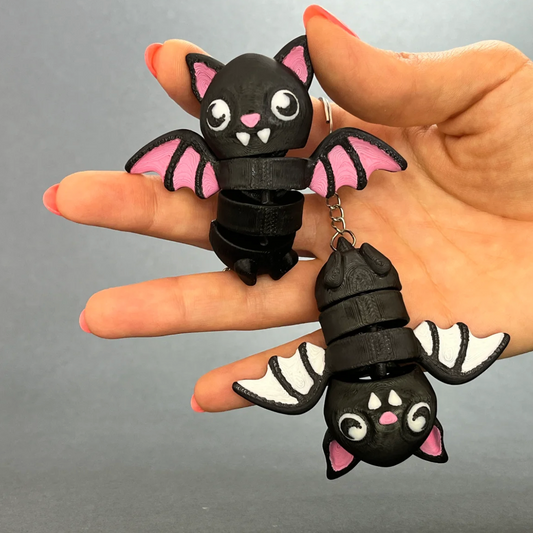 Flexi Halloween Bat keychains in Pink Wings and White Wings colorways, held in a hand